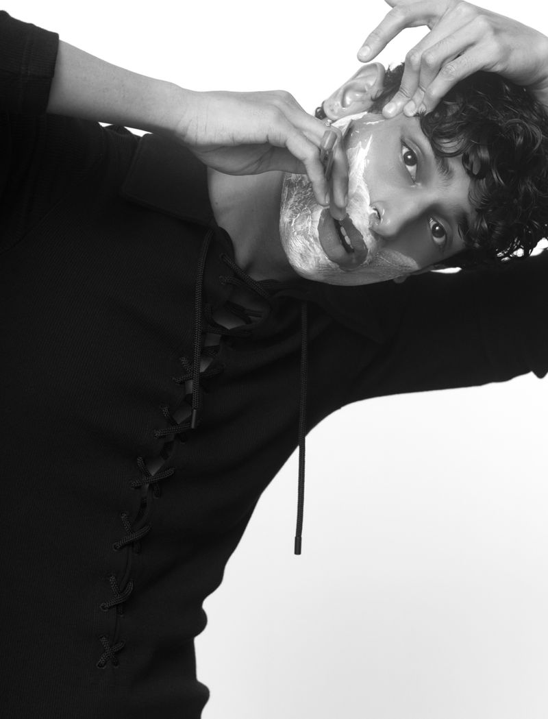 Monochrome portrait of an adult with cream on their face, leaning their head back while standing against a bright white backdrop.