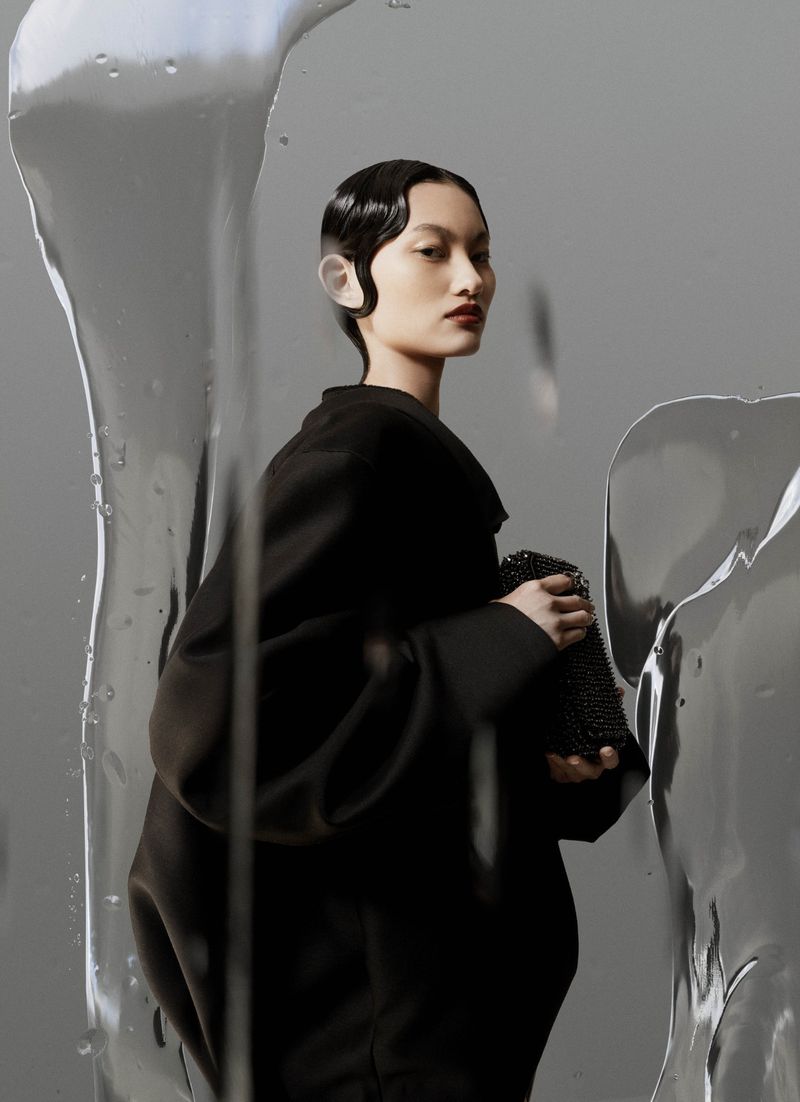 Asian woman with retro waves in dark clothing, holding a beaded purse, poses against gray with abstract ice block foreground.
