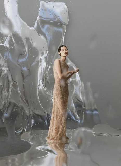 Elegant woman in embellished gown stands near abstract ice sculpture in a fashion photography studio. Focus on the gown and unique set design.