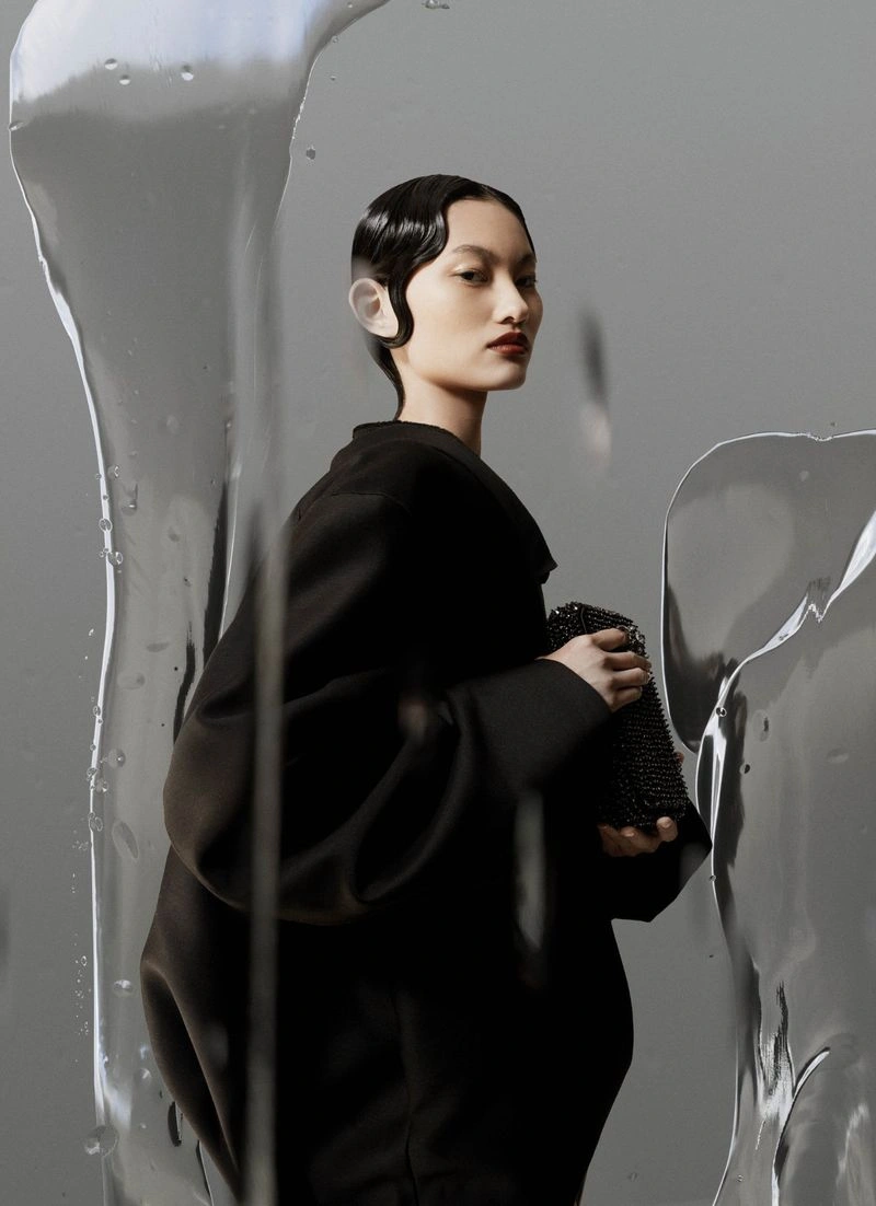 Model in black top holding a beaded clutch behind flowing liquid glass panels for Harper's Bazaar Australia editorial