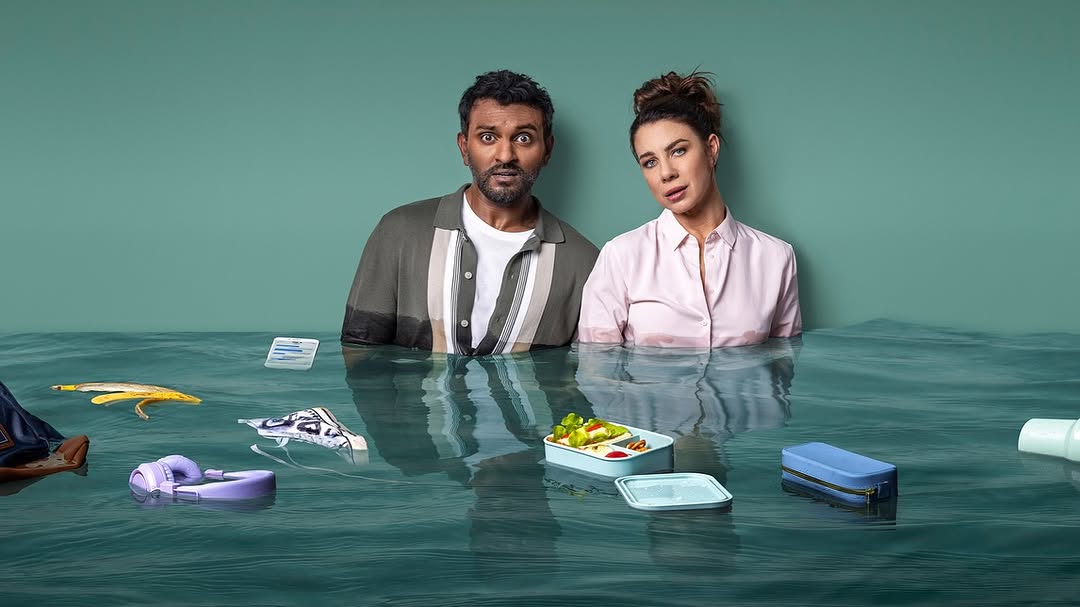 An adult man and woman are standing in water with various objects floating around them against an aqua background in a humorous image.