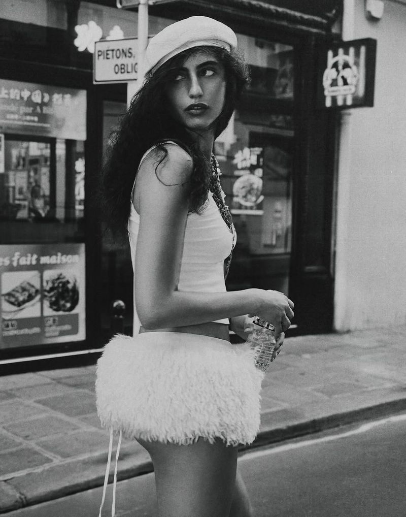 A woman in a white beret and a short white skirt is captured in a monochrome street-style photograph with a storefront backdrop.