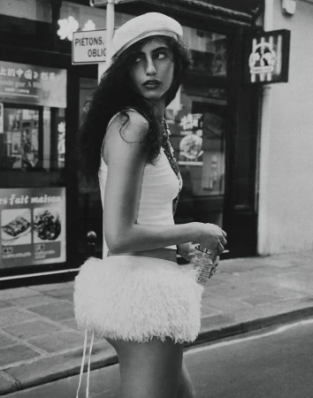 A woman in a white beret and a short white skirt is captured in a monochrome street-style photograph with a storefront backdrop.