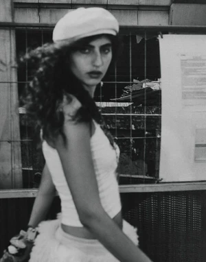 Model in white beret and tank top looking back in front of construction fencing for Vogue Adria