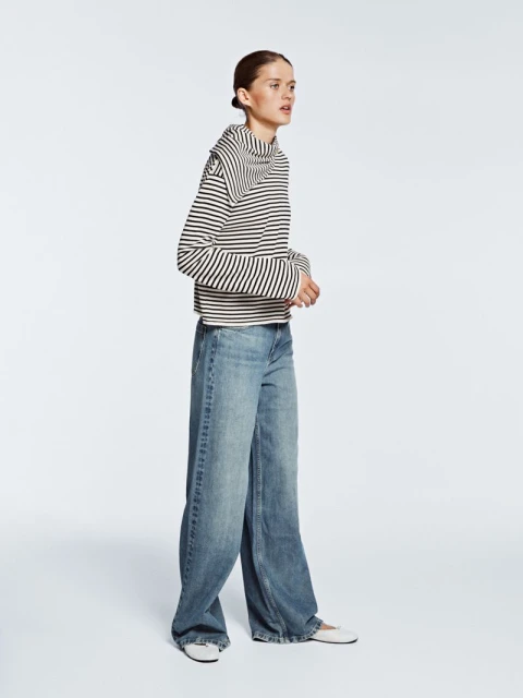 Fashion shot of a woman posing in a striped top and wide-leg denim jeans in a studio setting with a neutral background and diffused lighting.