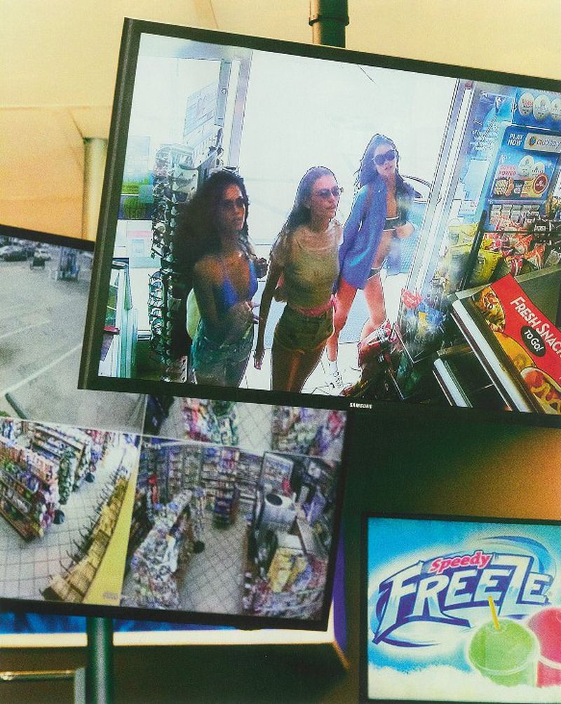 A television display showing three women posing in front of a store, with additional surveillance footage displayed on other screens.