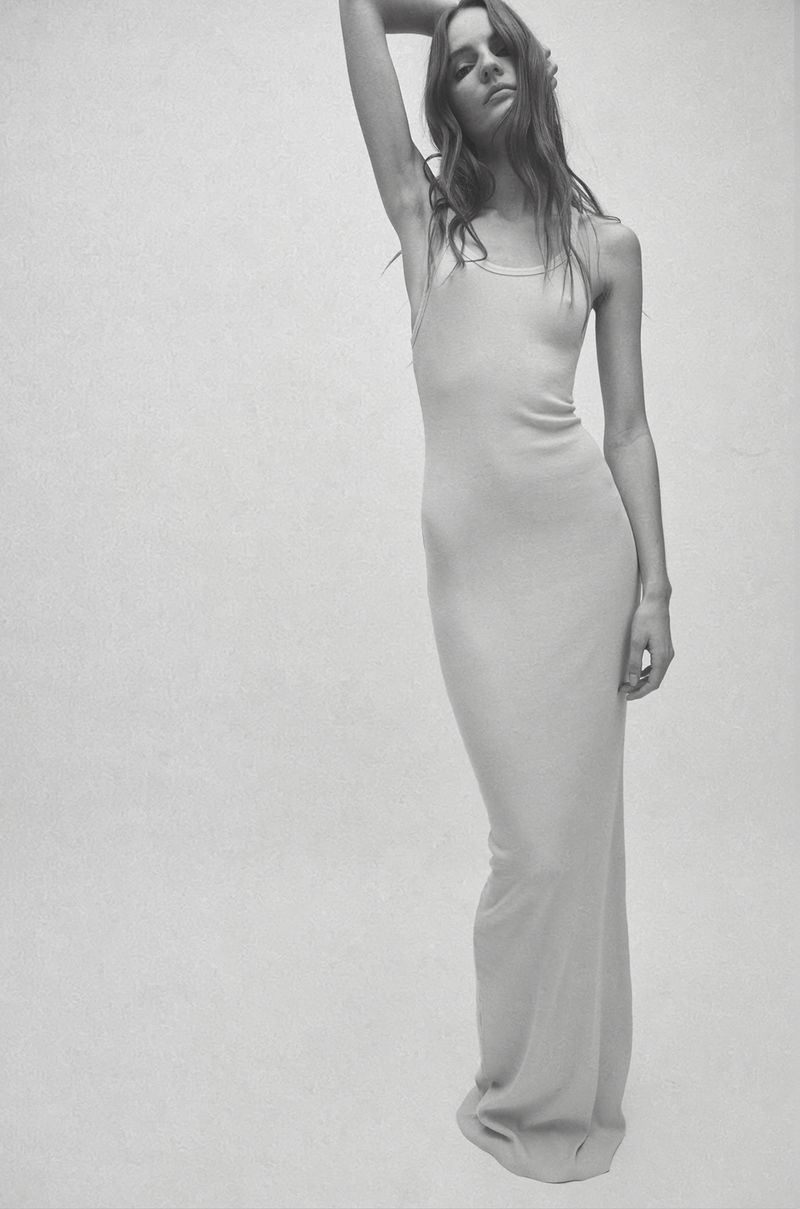Woman posing in a sleeveless maxi dress against a white background in a studio, emphasizing minimalist fashion and simple elegance.