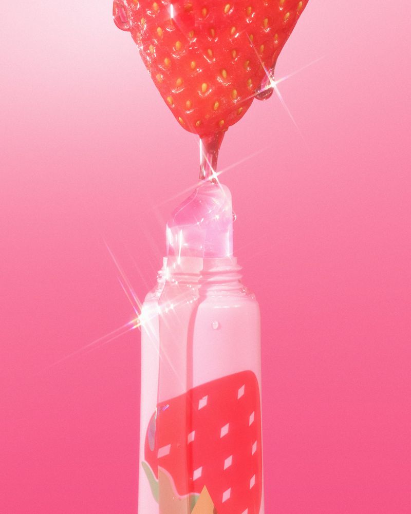 Strawberry lip gloss bottle with clear gloss dripping from a strawberry on top. Pink gradient background, beauty and makeup concept.