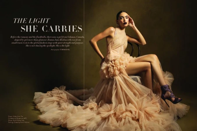 Elegant woman in ethereal gown poses seated in studio setting; fashion editorial with soft light, dark lipstick, and glamorous styling.