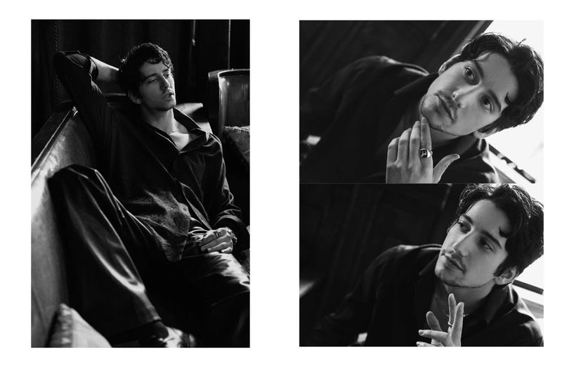 Monochromatic portrait of a young adult male in a dark shirt, relaxing on a sofa with a contemplative expression, indoors.