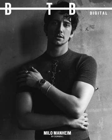 Black and white portrait of Milo Manheim on a magazine cover, arms crossed and wearing a dark sweater with metal chain detail.