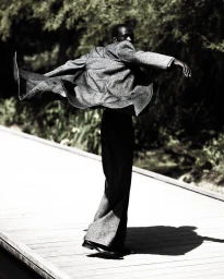 Model Hakim Deng in a textured grey jacket and trousers spinning on a wooden boardwalk in a high-contrast black and white shot.