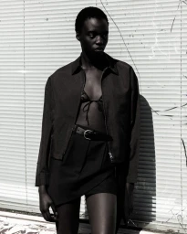 Model wearing a dark unzipped jacket over a black bra top and skirt against a ribbed shutter backdrop for Numero Netherlands.