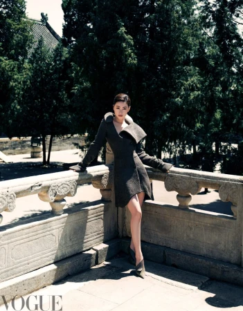 Actress Zhu Zhu leans against a carved stone balustrade wearing a structured dark coat dress and pointed heels for Vogue China.