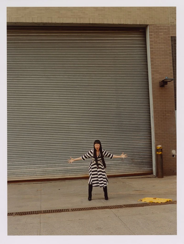 Model in a black and white striped dress and black boots standing in front of a large metal roller shutter door
