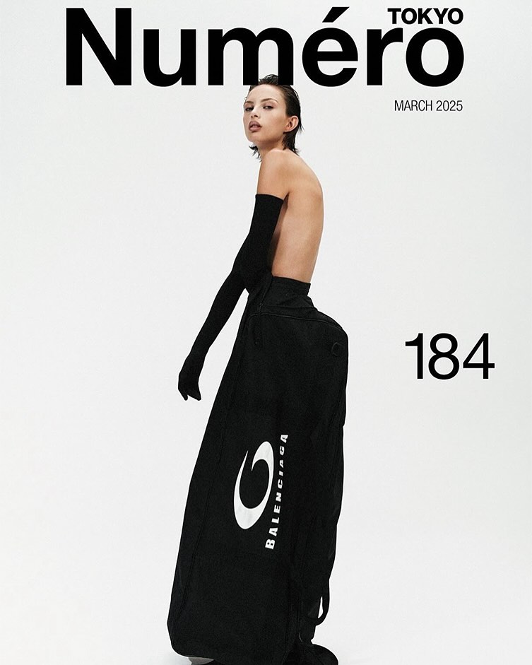 Fashion magazine cover featuring a slender adult female wearing black opera gloves and oversized black pants against a white background.