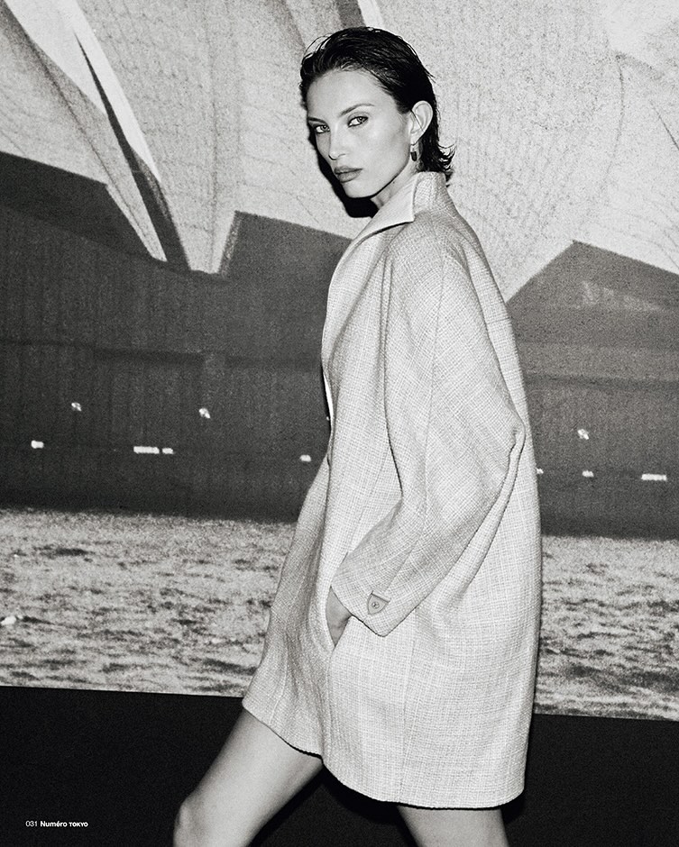 Black and white portrait of a woman wearing a structured coat against an architectural backdrop for Numero Tokyo.