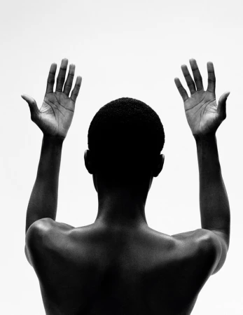 Back view of an African American adult with hands raised against a white background in a high-contrast, black and white photograph.