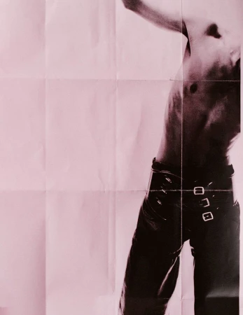 Artistic shot of a shirtless male torso and black leather pants against a pink paper background. Fashion and photographic style.