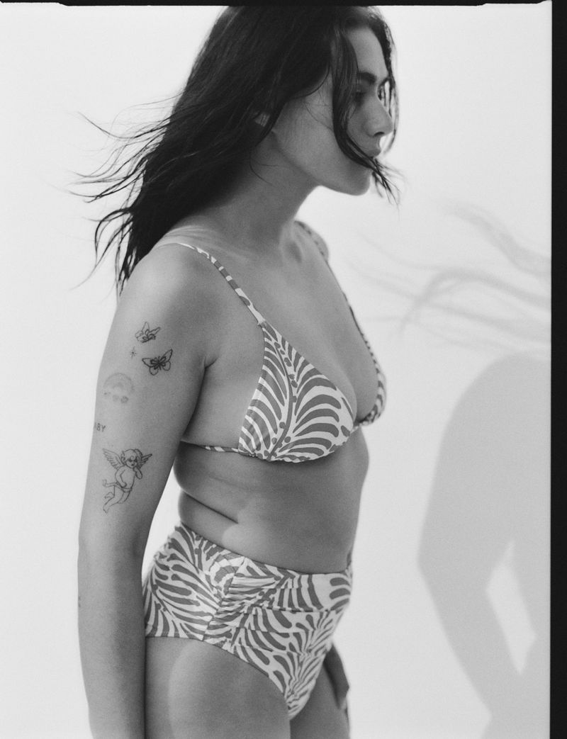 Monochromatic profile of a woman with dark hair, wearing a patterned bikini, standing indoors against a white backdrop with soft lighting.