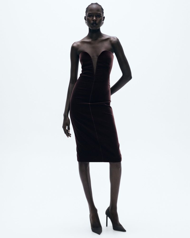 Elegant dark-skinned woman in a burgundy strapless midi dress and black heels, posing in a white studio. Fashion photography.
