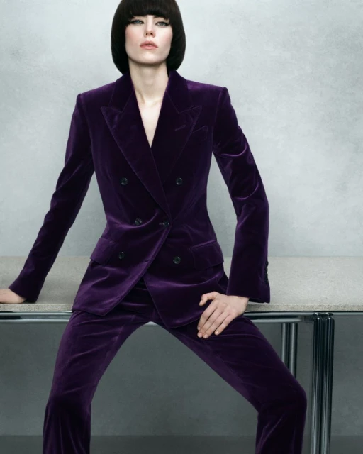 Adult female fashion model in a velvet purple suit posing indoors. Close-up, studio lighting, grey background. Beauty and fashion concept.
