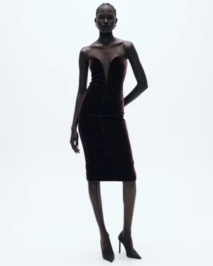 Model wearing a strapless dark burgundy velvet midi dress with black stiletto heels against a white seamless studio background.