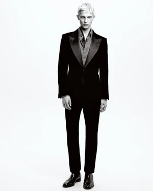 Blonde male model wearing a black velvet tuxedo jacket and trousers against a white background