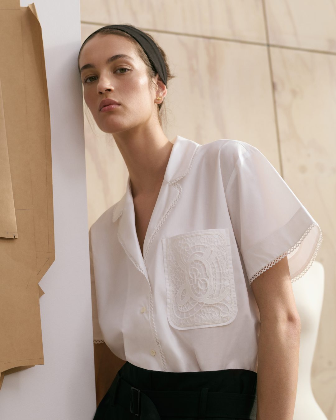 A stylish woman with a headband poses in a white shirt with lace details, complemented by a mannequin and crafting patterns.
