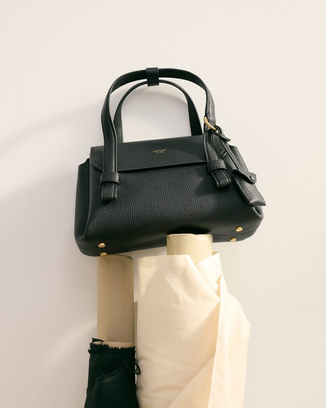 Black leather handbag with top handles and gold accents on a white surface with rolls of fabric, fashion accessory, studio shot.