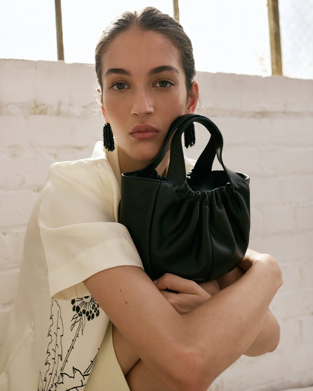 Portrait of a woman with a black purse indoors, dressed in a white shirt, showcasing beauty and fashion in a neutral setting.