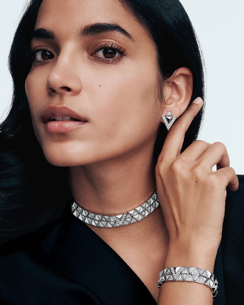 Close-up of a woman showcasing jewelry: choker, bracelet, and earrings, set against a clean, light background, emphasizing elegance and design.