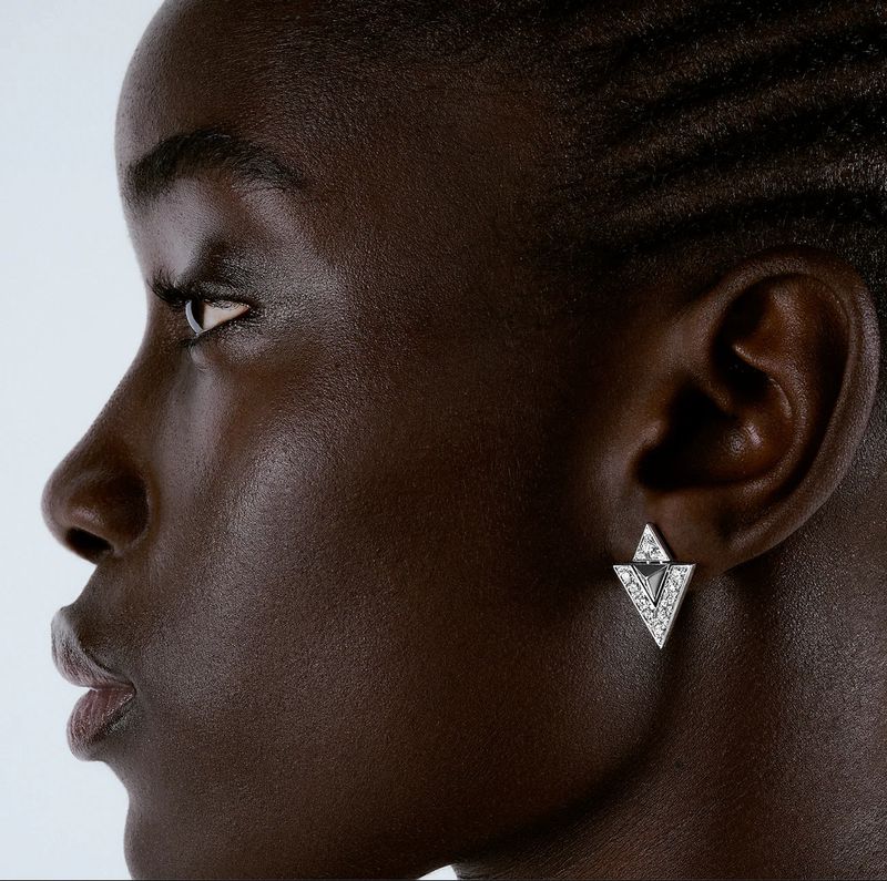 Close-up profile of a dark-skinned adult female with short, neatly styled hair and wearing triangle-shaped earrings with small gemstones.