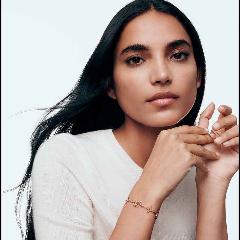 Portrait of an adult female wearing a light-colored sweater and a thin metallic bracelet with decorative shapes, against a white background.
