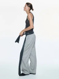 Profile view of a female model wearing a dark sleeveless top, grey trousers, and a sweater tied around her waist against a white background.
