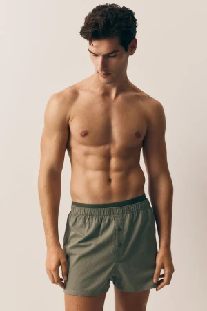 Handsome, muscular man in boxer shorts poses in a studio. Healthy lifestyle portrait showcases the male form with neutral background.