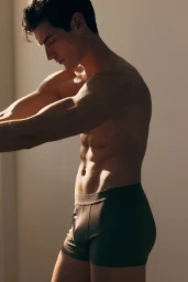 Profile portrait of a male model wearing dark boxer briefs against a neutral background with warm directional lighting.