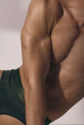 Close-up of a muscular male model wearing dark green underwear against a clean white backdrop.