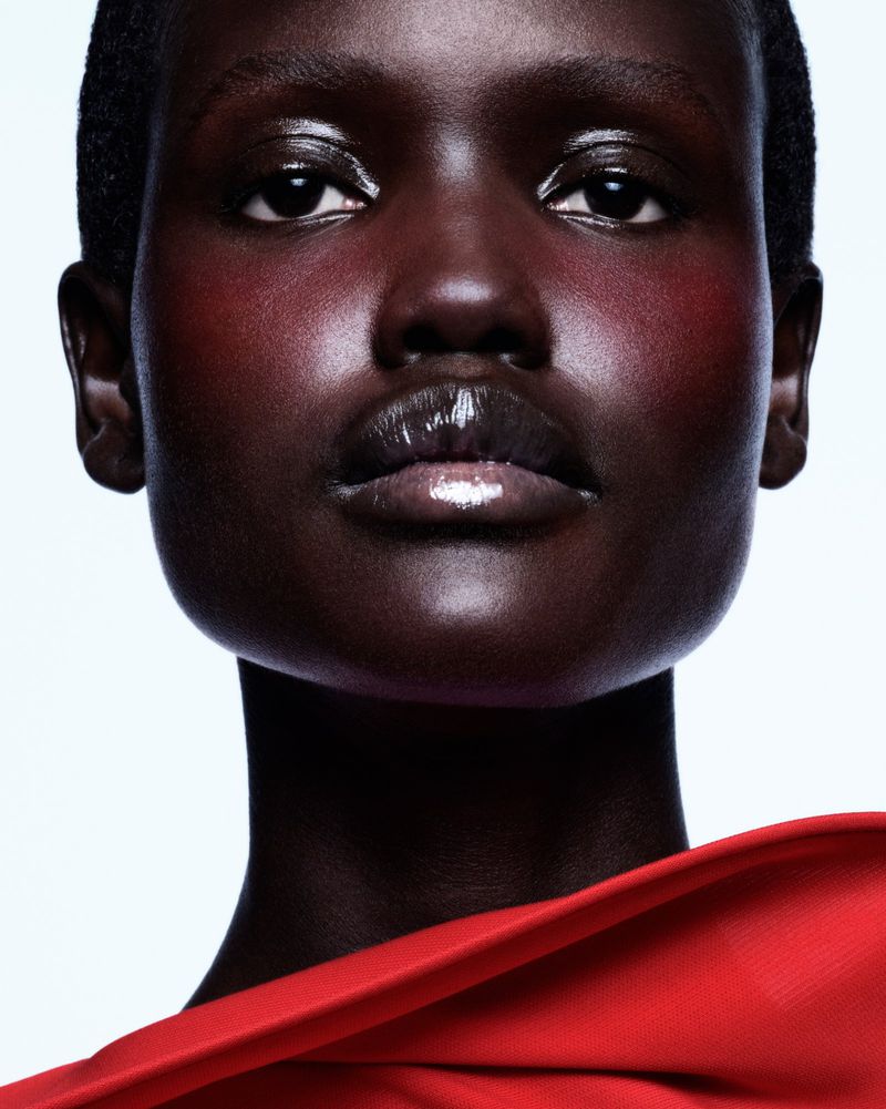 Close-up portrait of a dark-skinned woman with glossy lips and a red fabric drape against a neutral background, beauty shot, studio lighting.