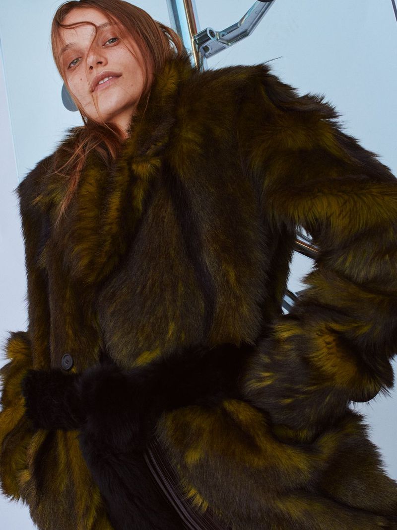 A woman wearing a patterned fur coat with a light blue wall background and silver, metallic fixtures.