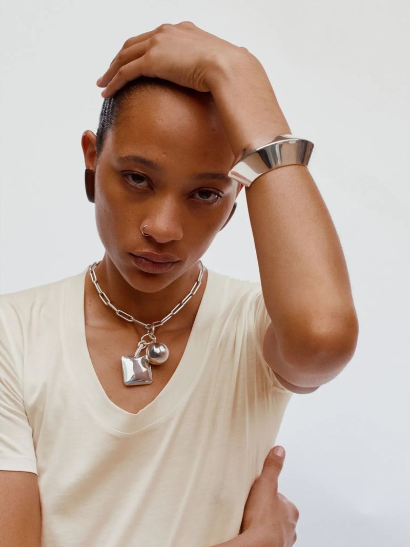 Woman poses with silver bracelet and chain necklace against a white backdrop in a fashion or beauty shot for Visie.