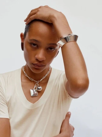 Woman poses with silver bracelet and chain necklace against a white backdrop in a fashion or beauty shot for Visie.