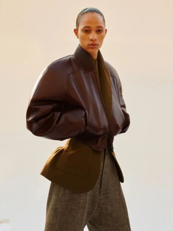 Fashionable adult woman poses in a studio wearing a brown leather jacket with green wool lining and tweed pants for a portrait.