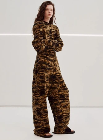 Fashionable woman in patterned knitwear outfit poses in studio, illuminated by soft lighting, showcasing modern apparel and style trends.