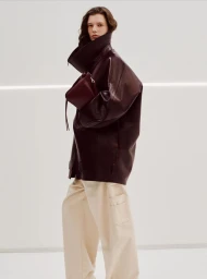 Model wearing a dark oversized leather jacket and cream trousers against a white seamless background