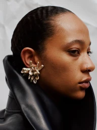 Close-up profile portrait of a model wearing a sculptural metallic ear cuff and a black leather collar against a white background