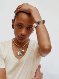 Model wearing a chunky silver cuff bracelet, pendant necklace, and cream top against a seamless white background.