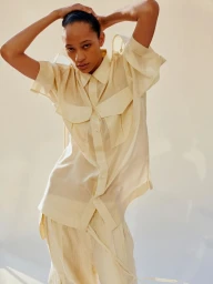 Model posing with hands behind head wearing a light yellow button-down shirt against a neutral background