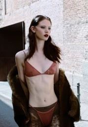 Model in underwear and a brown fur coat standing outside against a brick wall for an editorial by Bryan Torres.