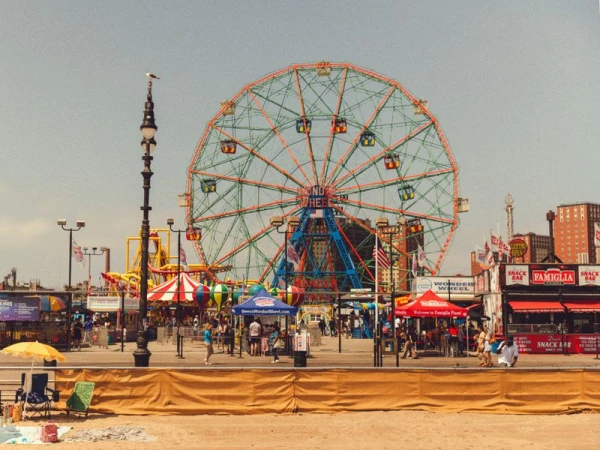 Scenic view of the Wonder Wheel at Coney Island with people, vendor kiosks, and beach in the foreground on a clear day.